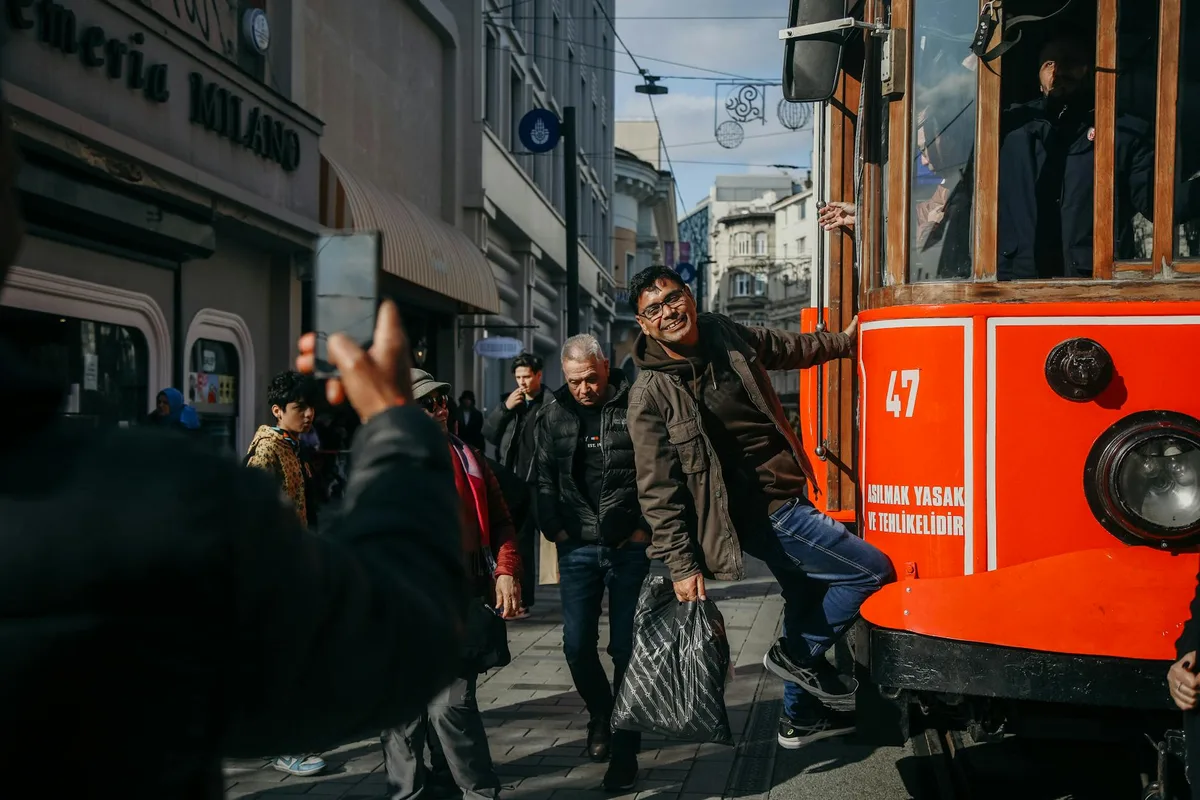 Uomo sul famoso tram rosso di Istanbul su Istiklal Caddesi, momento gioioso di viaggio urbano.