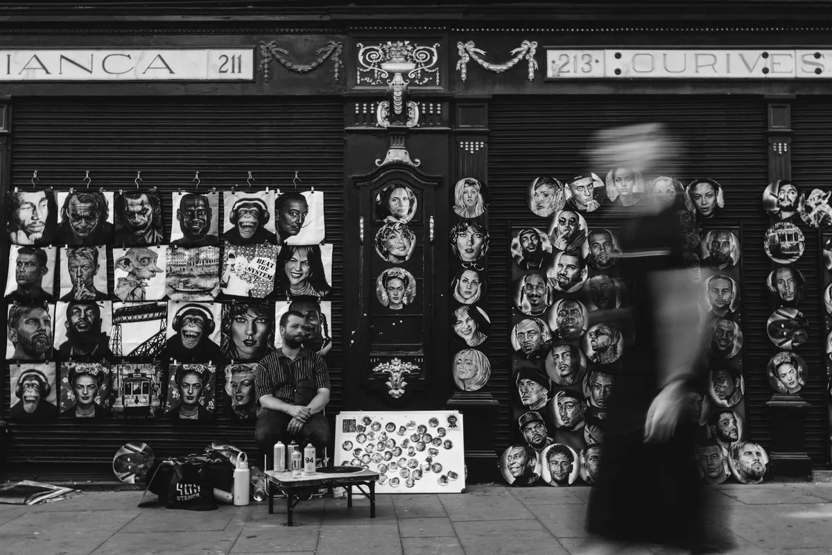 Schwarz-Weiß-Foto eines Straßenkünstlers mit Porträts in Porto, Portugal