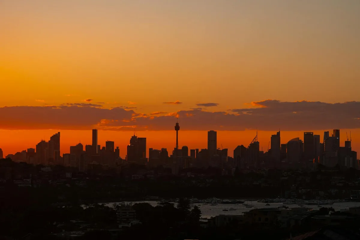 Atemberaubende Sydney-Skyline als Silhouette vor leuchtend orangefarbenem Sonnenuntergangshimmel