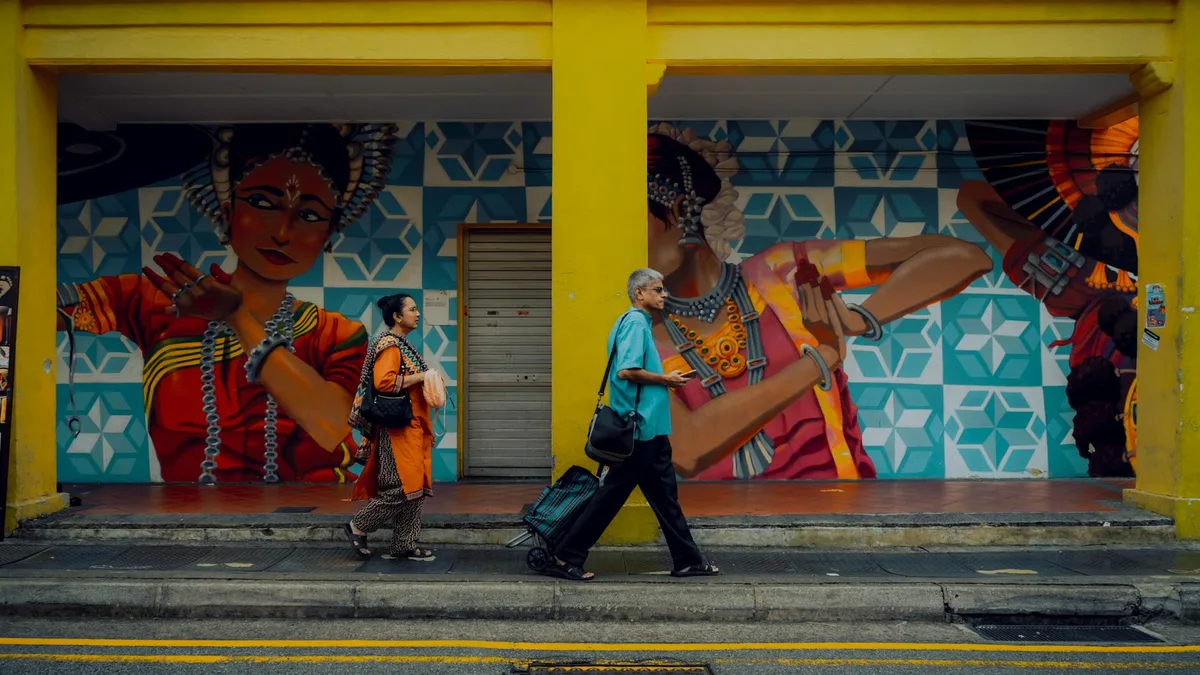Pareja caminando con bolsos junto a mural callejero en Singapur