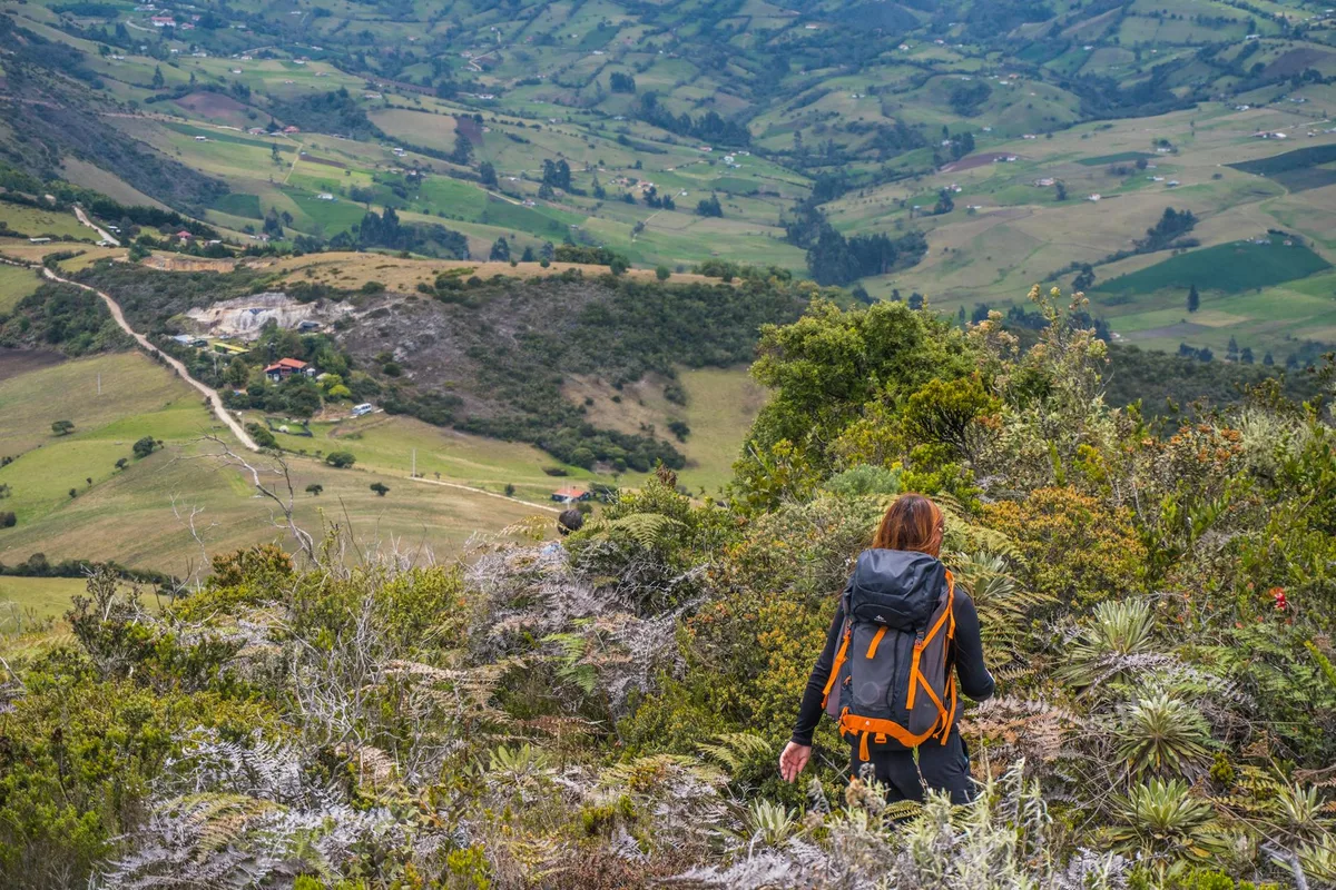 Mujer con mochila haciendo senderismo en paisajes verdes de Guatavita, Colombia