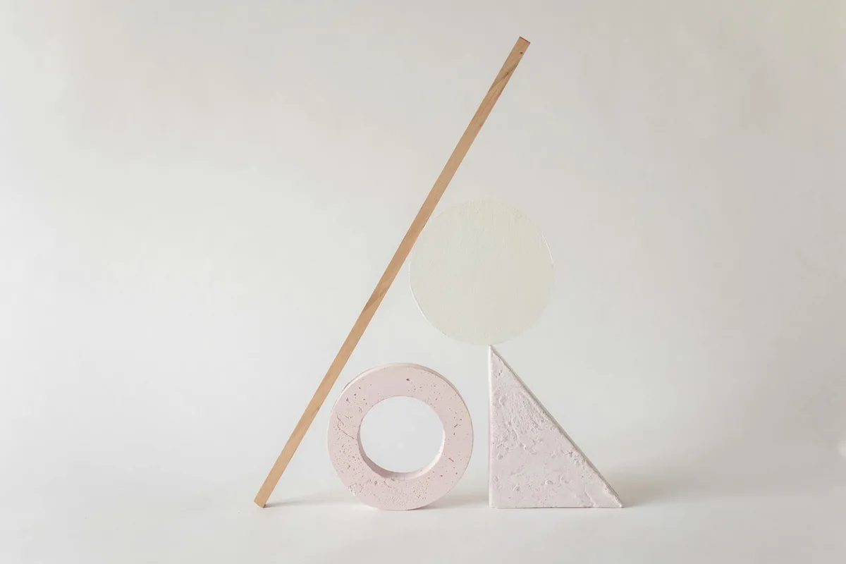 Disposizione minimalista elegante di forme geometriche astratte su sfondo neutro chiaro.