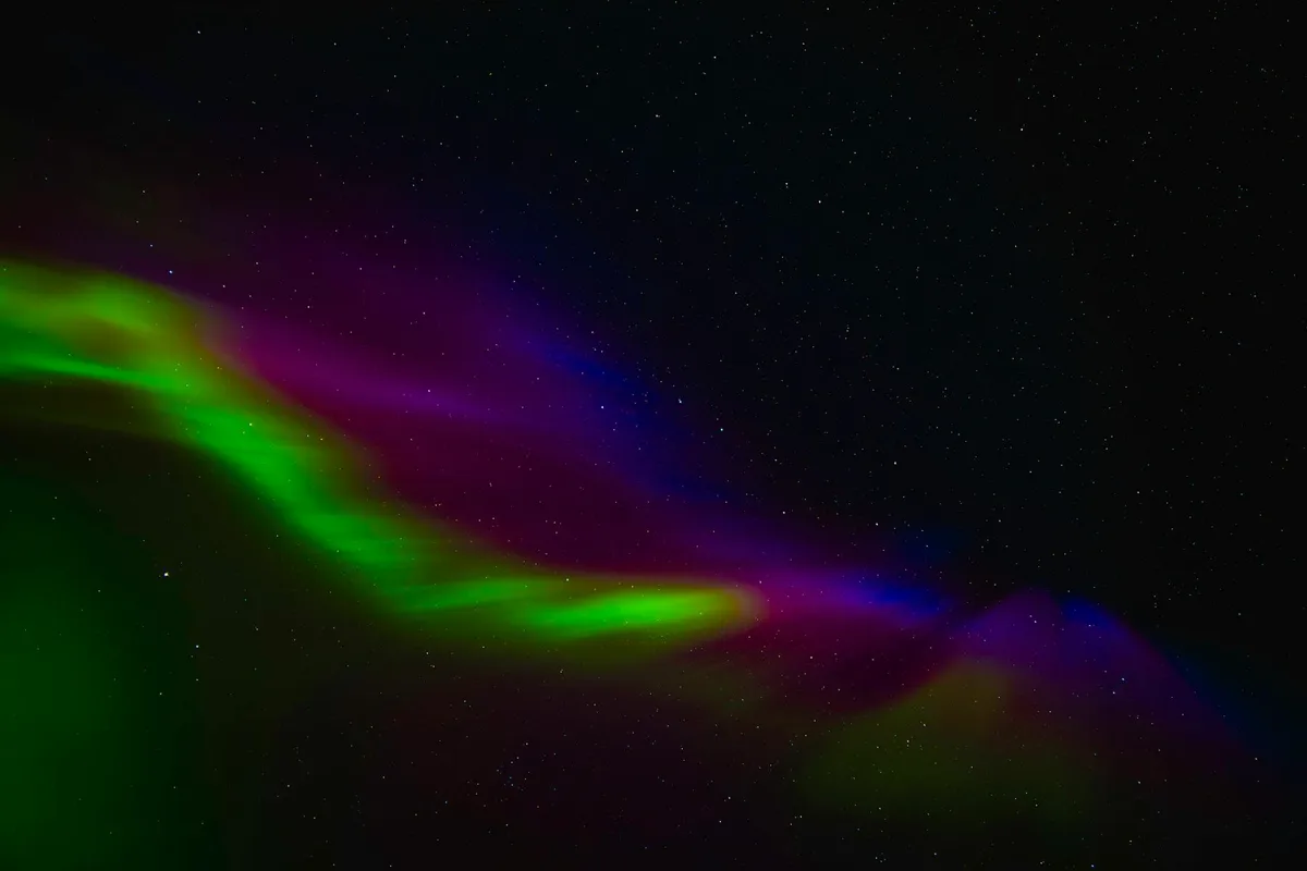 Aurora boreale, vividi verdi, rosa e blu su cielo norvegese.