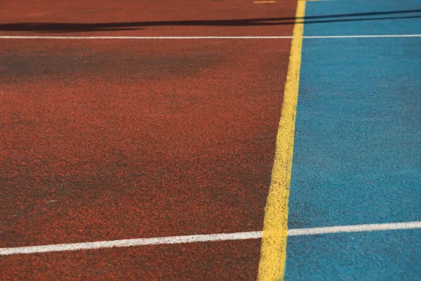 Vivid sports court with red and blue surfaces separated by a yellow line.