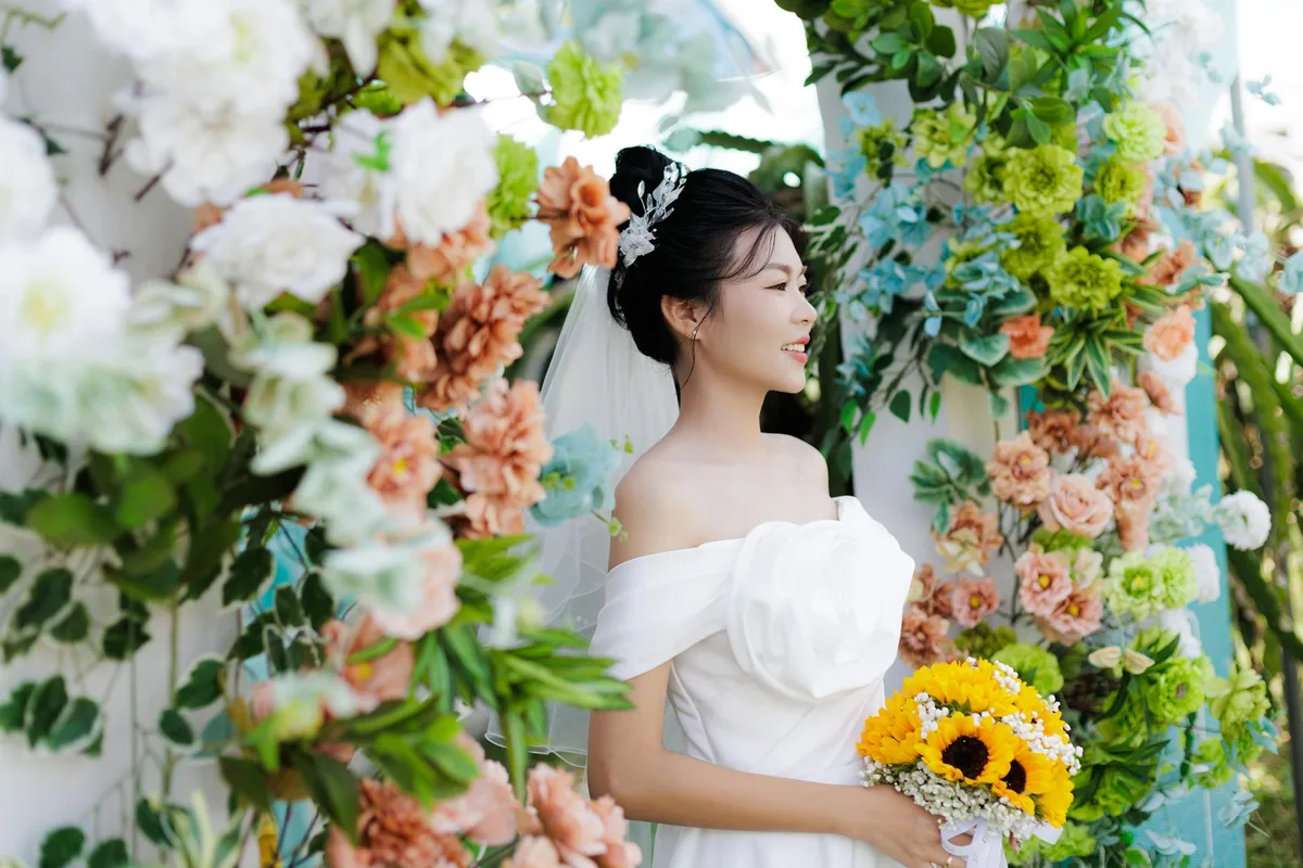 Wunderschöne Braut im weißen Kleid steht zwischen bunten Blumen und verkörpert Eleganz und Freude
