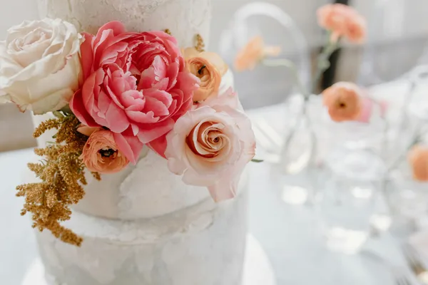 A beautifully decorated wedding cake adorned with pink and white roses and peonies, perfect for a romantic celebration.