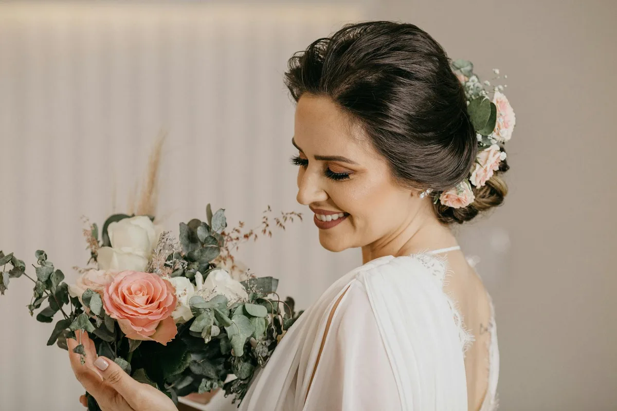Braut im weißen Kleid mit Blumenstrauß und eleganter Hochsteckfrisur lächelnd