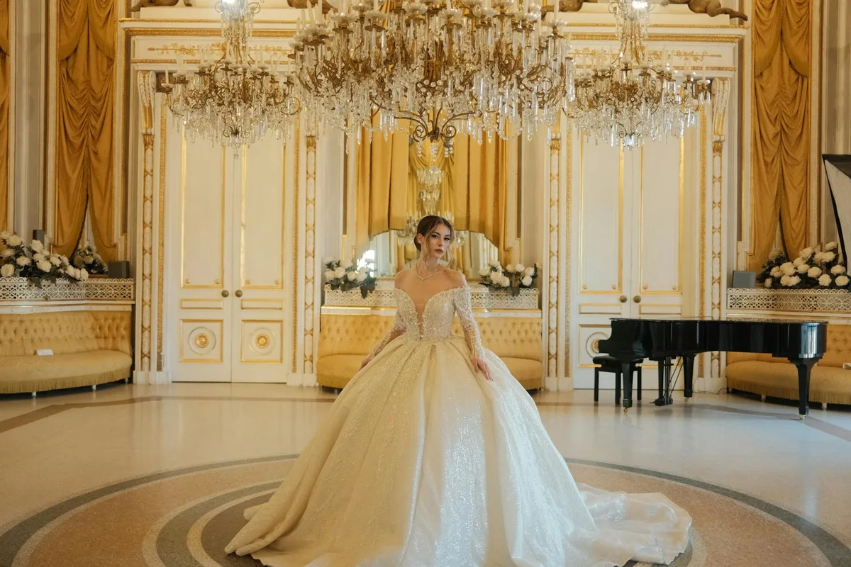 Braut im eleganten Kleid vor Kronleuchter und Klavier im luxuriösen Ballsaal