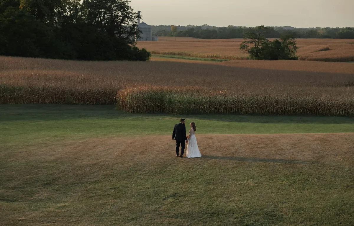 Coppia in abito nuziale mano nella mano in un paesaggio rurale sereno al tramonto