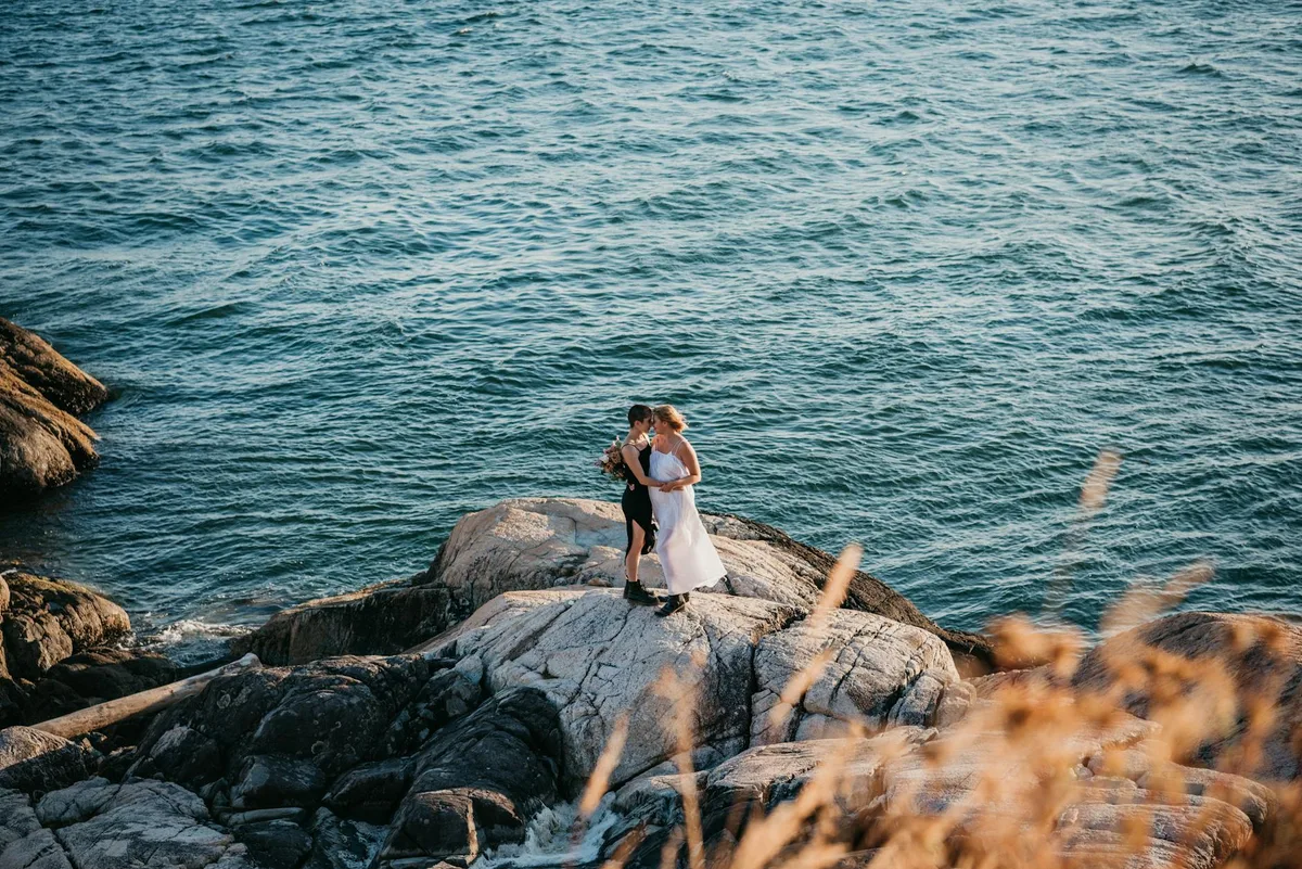 Liebevolles Paar umarmt sich auf felsigen Klippen am Meer bei Sonnenuntergang
