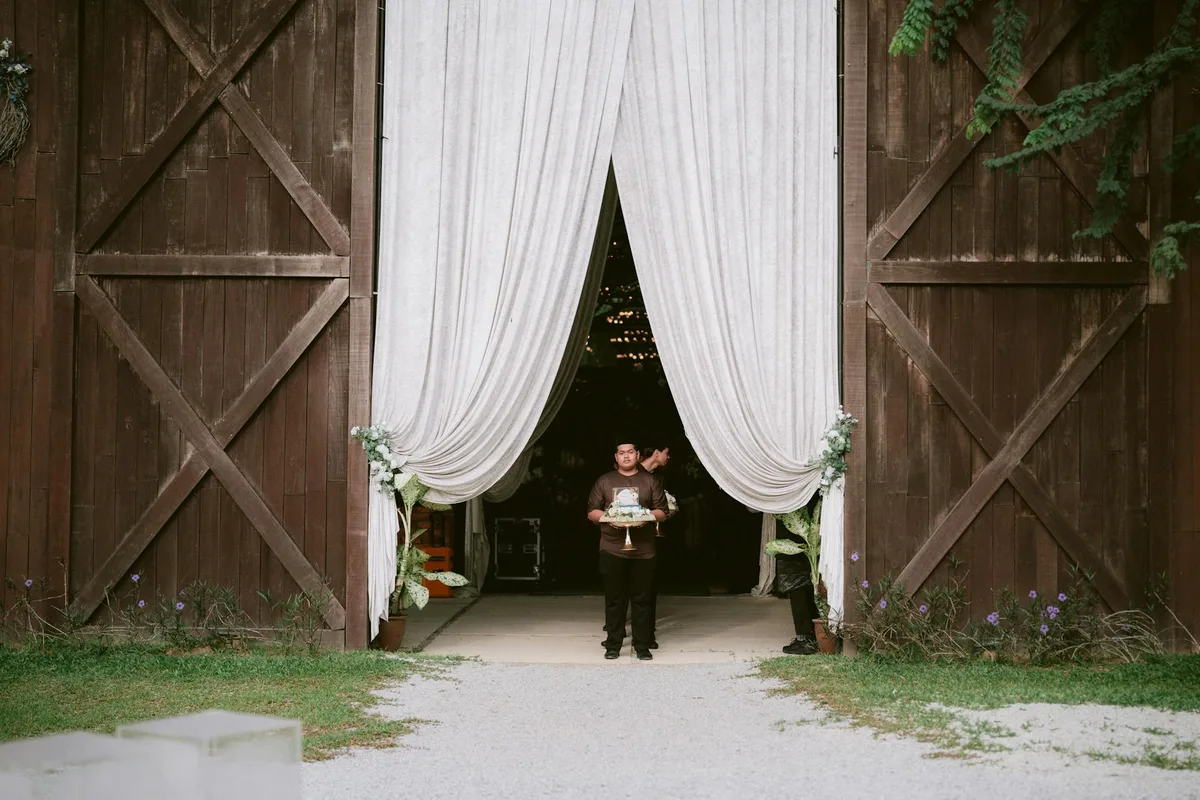 Pessoa com bolo na entrada de celeiro rústico com cortinas abertas, evento festivo