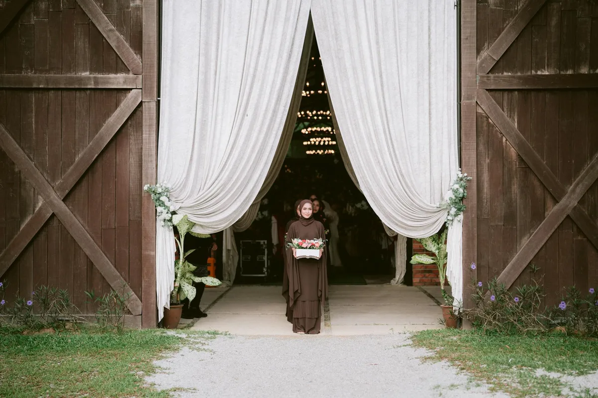 Sposa in abito marrone con fiori all'ingresso di un venue rustico