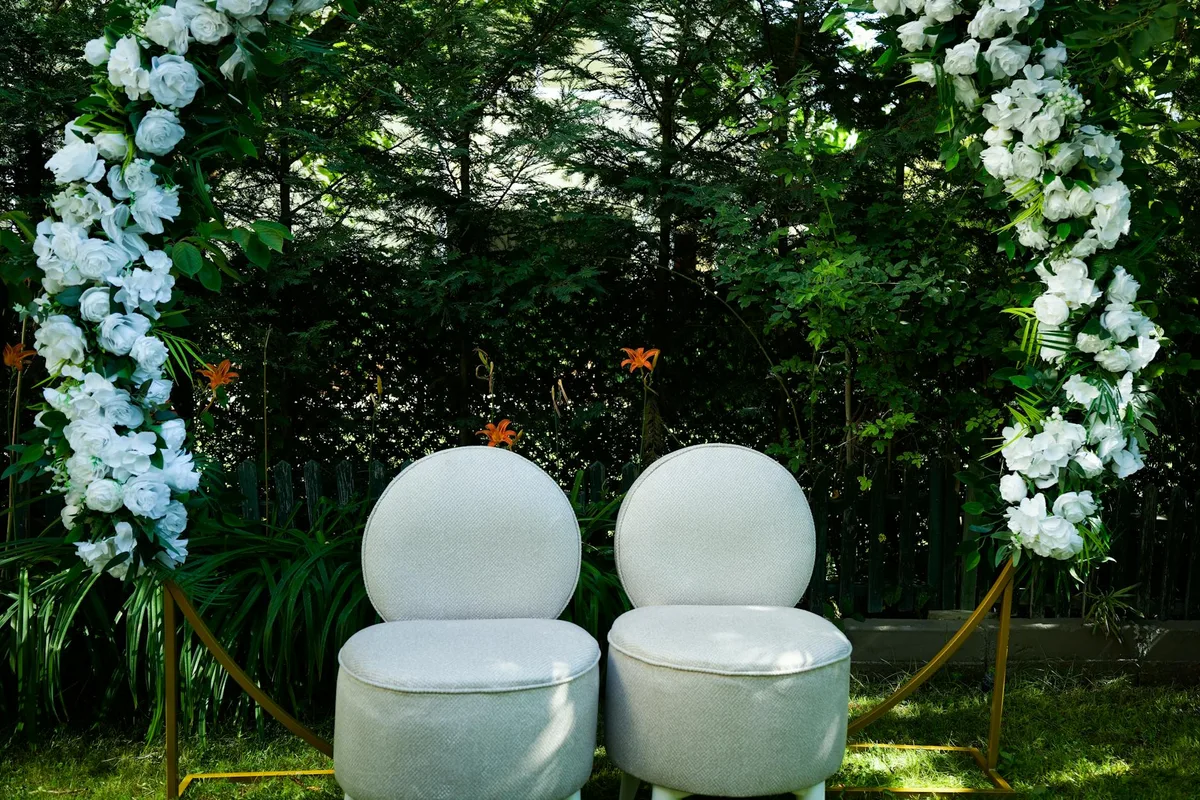 Hochzeitszeremonie mit Blumenbogen und weißen Stühlen