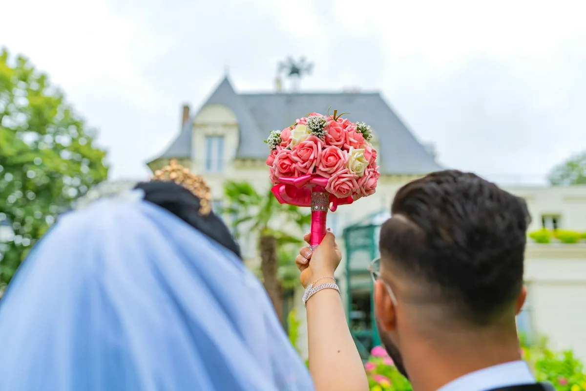 Brautpaar feiert Hochzeitstag mit Blumenstrauß auf malerischem Schloss in Paris, Frankreich
