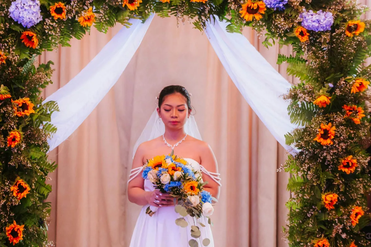 Sposa sotto un arco floreale vibrante con bouquet di fiori misti
