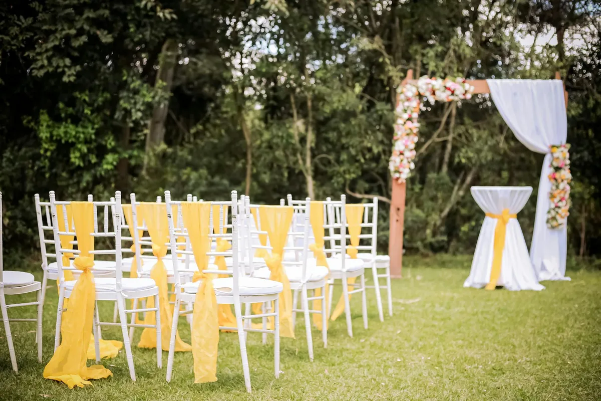 Charmante Outdoor-Hochzeit mit Blumenbogen und weißen Stühlen mit gelben Schärpen