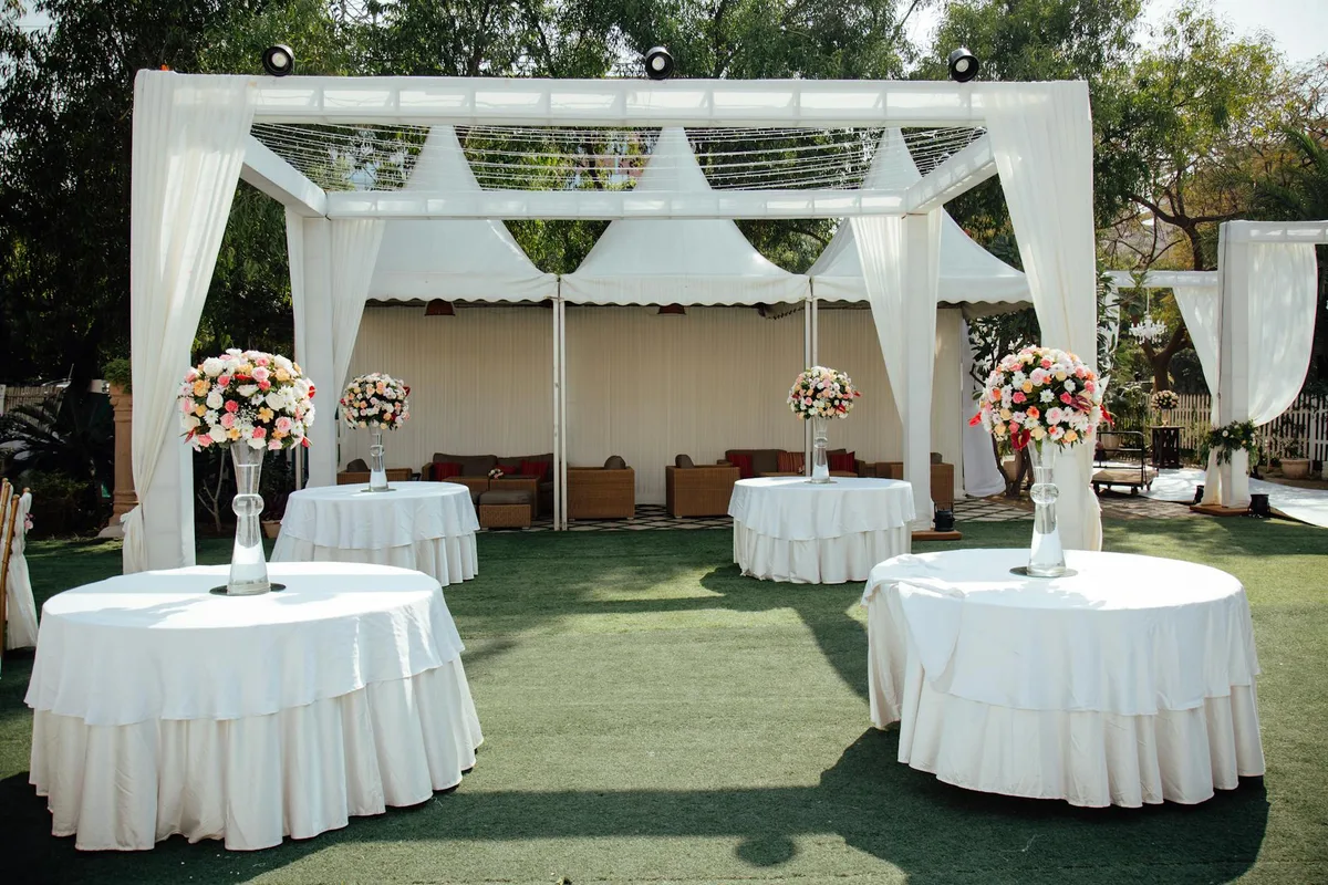 Charmante Outdoor-Hochzeit mit weißen Pergolen und Blumenarrangements unter sonnigem Himmel
