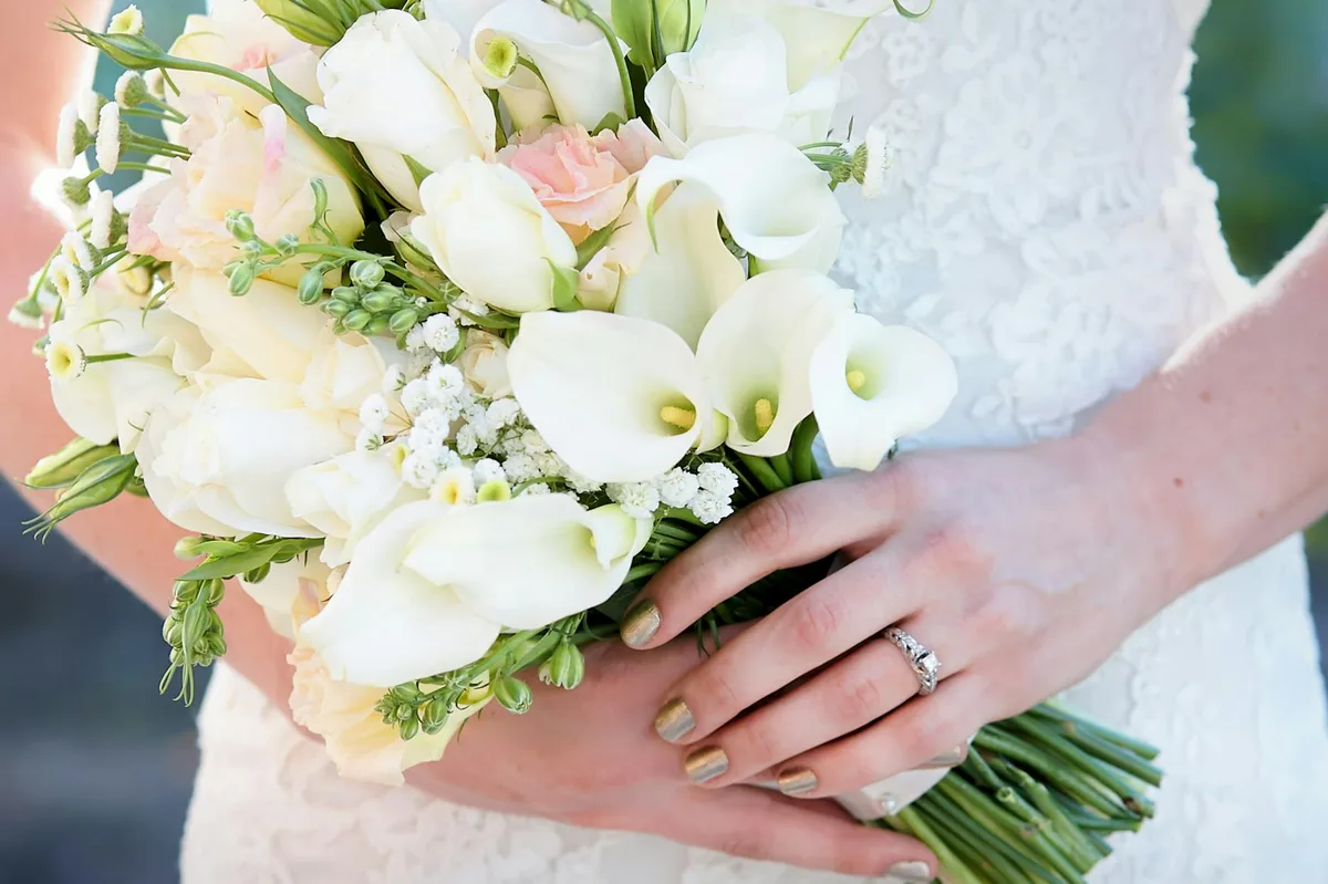 Primo piano di bouquet nuziale elegante con calle e rose, tenuto dalla sposa