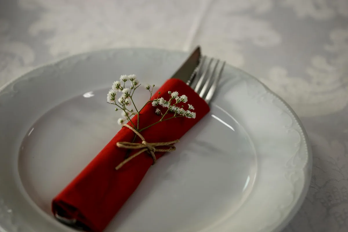 Elegante Tischdekoration mit roter Serviette, Besteck und weißen Blumen für ein edles Dinner