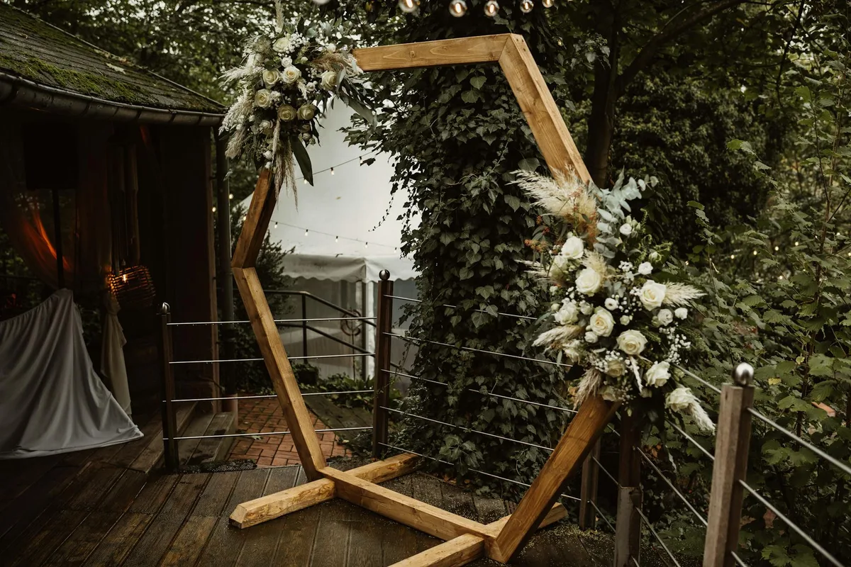 Eleganter Holzbogen mit weißen Blumenarrangements in üppiger Outdoor-Umgebung
