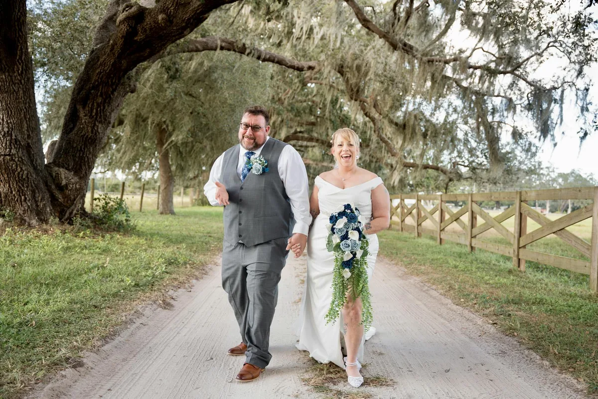 Glückliches Paar spaziert unter üppigen Bäumen und hält sich an den Händen an ihrem Hochzeitstag.