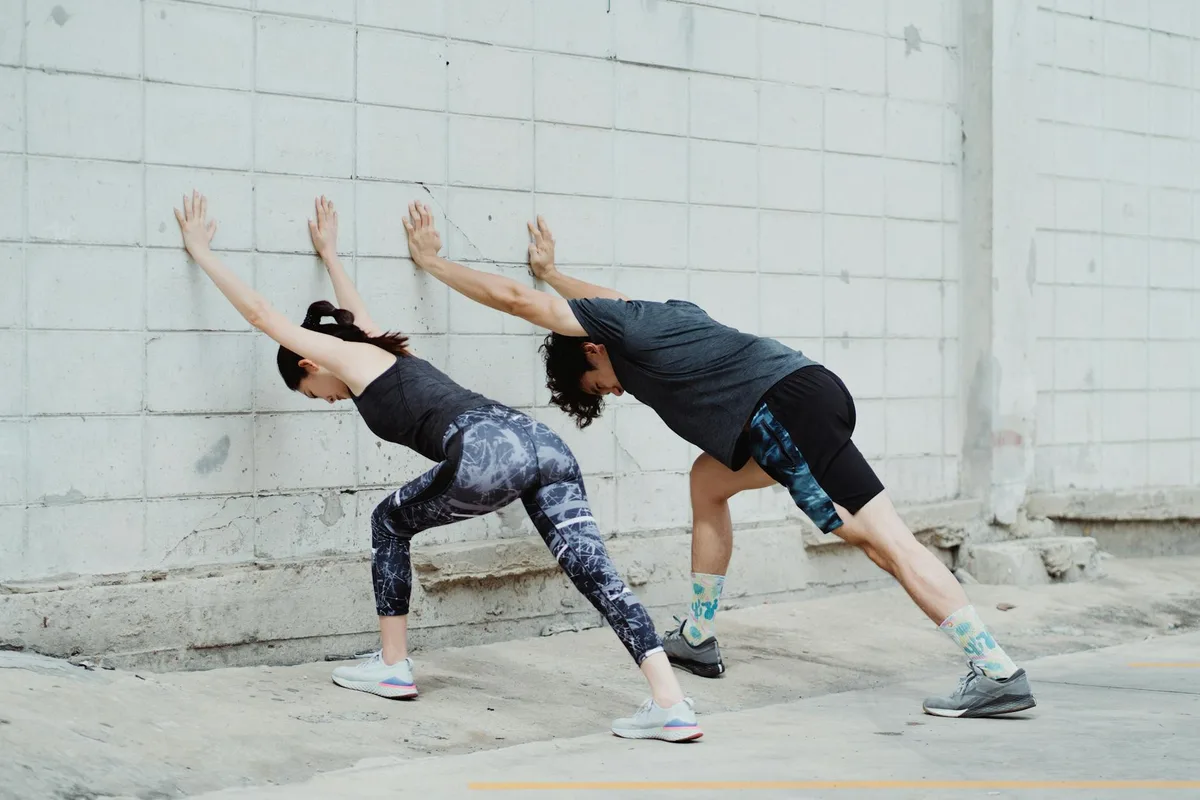 Una pareja se estira al aire libre sobre una superficie de concreto, destacando el ejercicio y el fitness urbano.