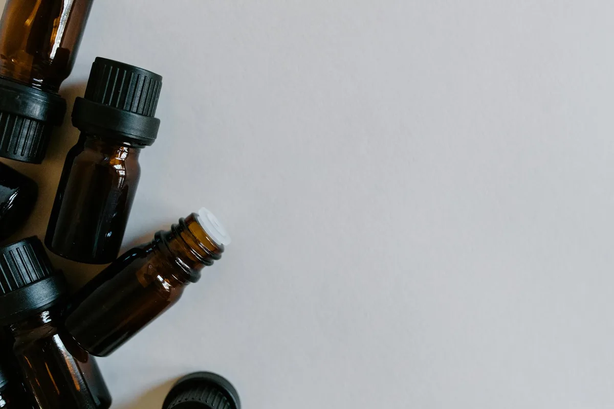 Bottiglie di olio essenziale marroni in composizione minimalista su sfondo bianco per aromaterapia