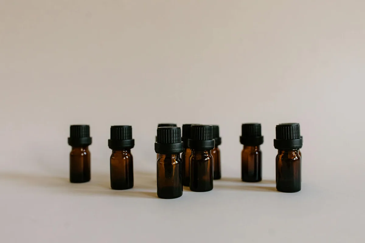 Minimalistisches Stillleben mit mehreren bernsteinfarbenen Duftölflaschen mit schwarzen Verschlüssen auf neutralem Hintergrund.