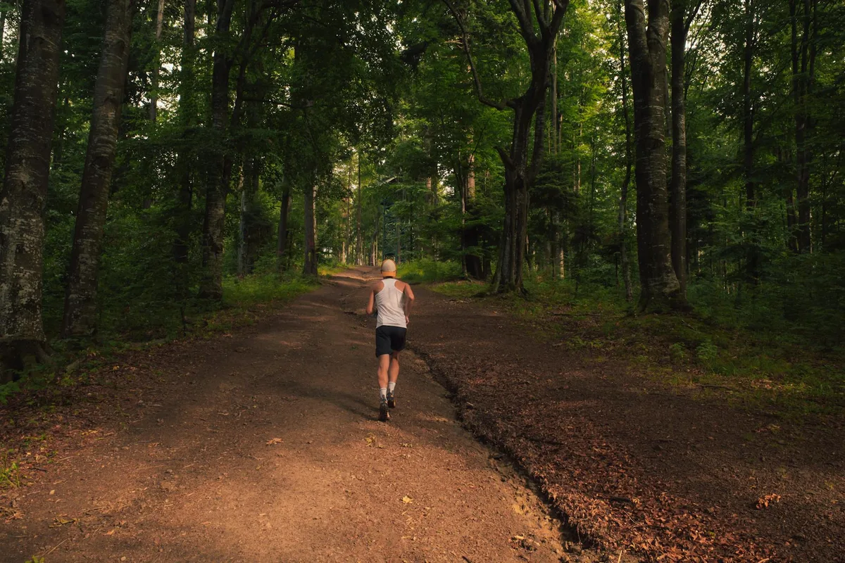 Eine Person joggt auf einem unbefestigten Weg durch einen üppigen grünen Wald am Tag.