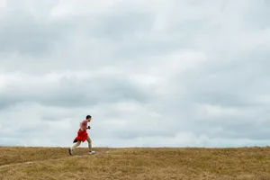 Adult male jogging on a grassy trail during the day with overcast skies. Ideal for fitness and lifestyle themes.