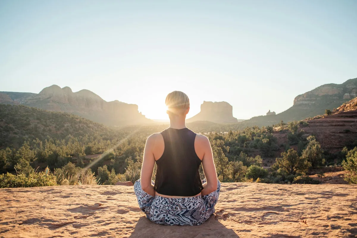 Retro di donna in abbigliamento estivo che medita in Padmasana su scogliera illuminata all'alba