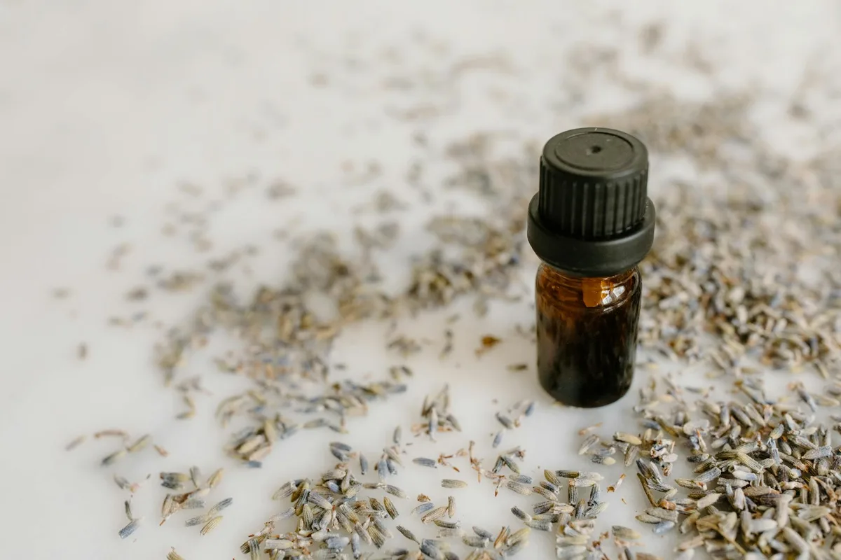 Nahaufnahme einer braunen Glasflasche mit Lavendelöl, umgeben von getrockneten Lavendelblüten