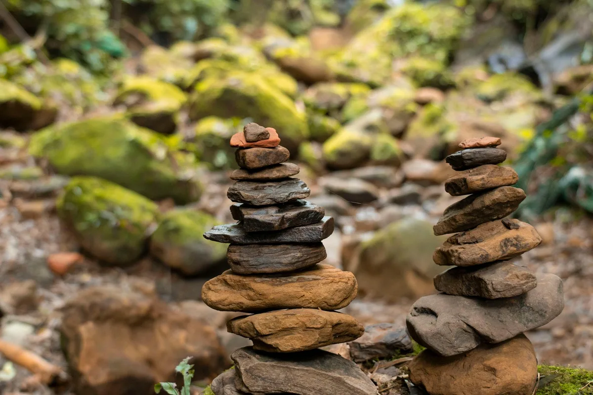 Primo piano di cairn di pietra impilati in una foresta muschiosa, che evidenzia l'equilibrio naturale.