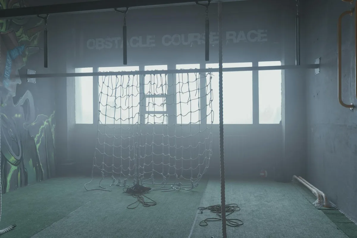 Indoor gym featuring a cargo net and ropes for obstacle course training.