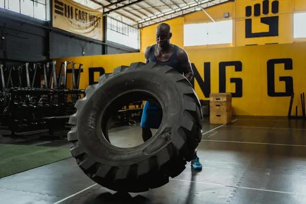 Muscular man exercising with large tire for strength training in a gym.