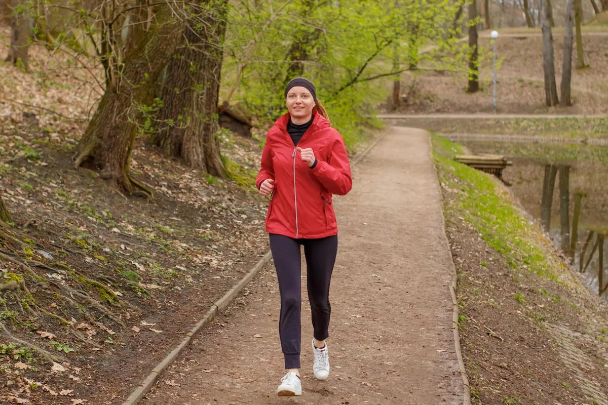 Frau in roter Jacke joggt auf einem Waldweg im Frühling.