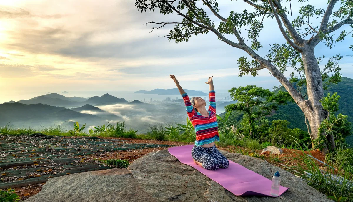 Donna che pratica yoga all'alba in natura su una collina con una bella vista montagna